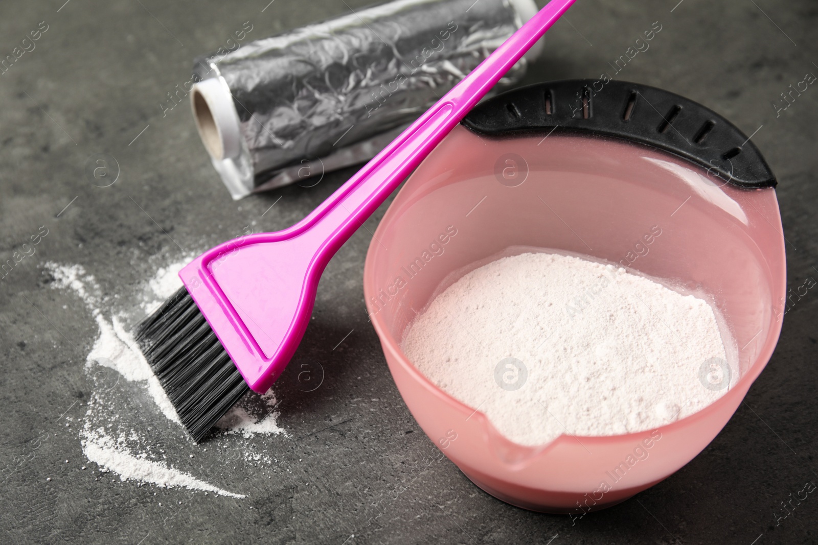 Photo of Bowl with hair dye, brush and foil on grey stone table, closeup