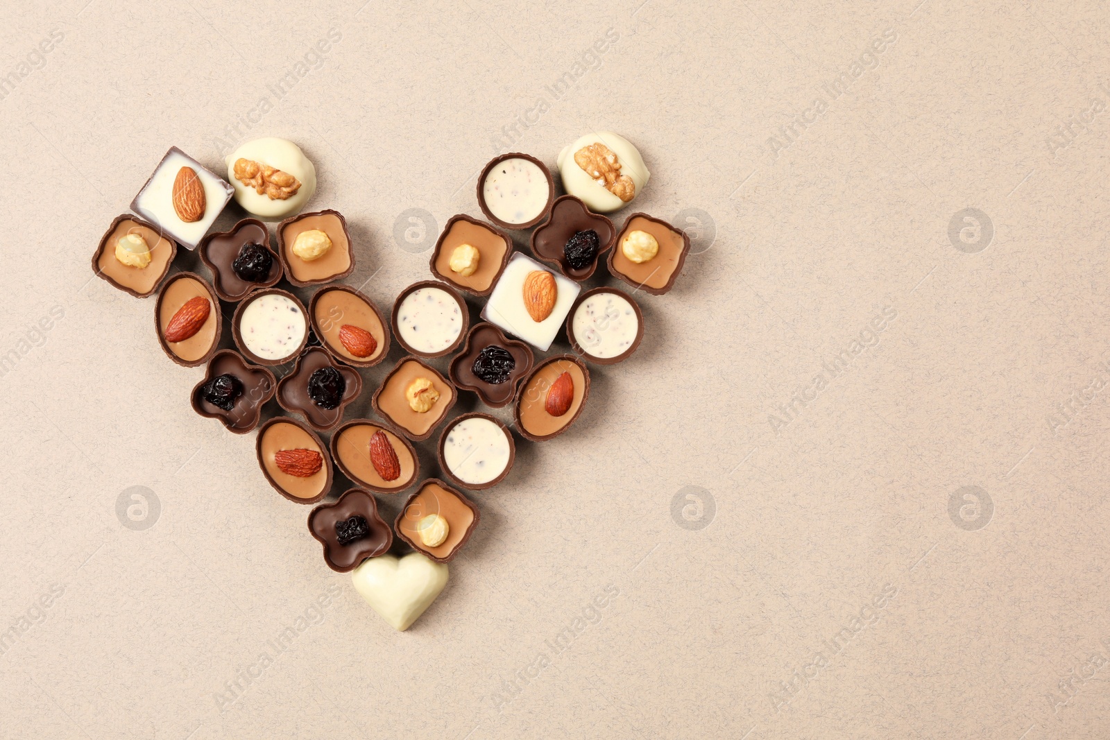 Photo of Heart made with delicious chocolate candies on beige background, top view. Space for text