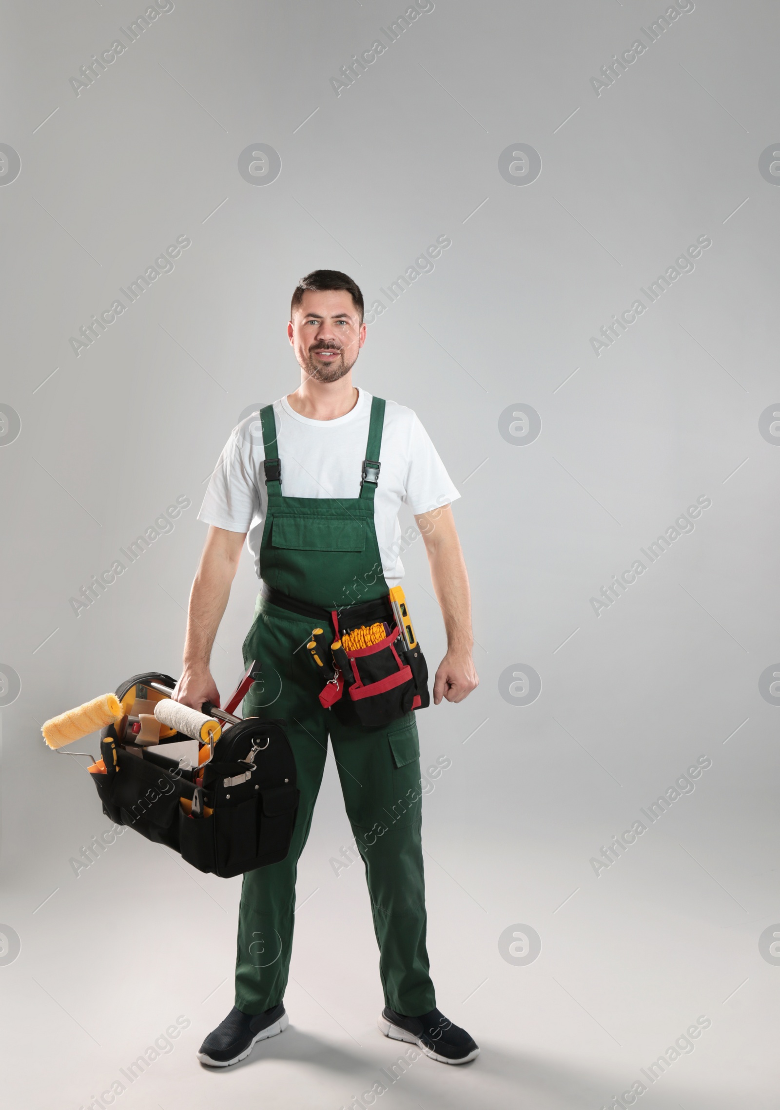 Photo of Full length portrait of professional construction worker with tools on grey background