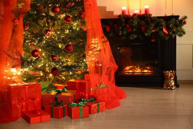 Photo of Beautifully wrapped gift boxes under Christmas tree near fireplace in living room