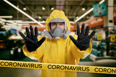 Image of Man in chemical protective suit showing STOP gesture indoors. Prevention of virus spread
