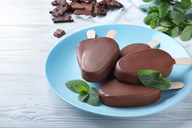 Plate with glazed ice cream bars and fresh mint on white wooden table