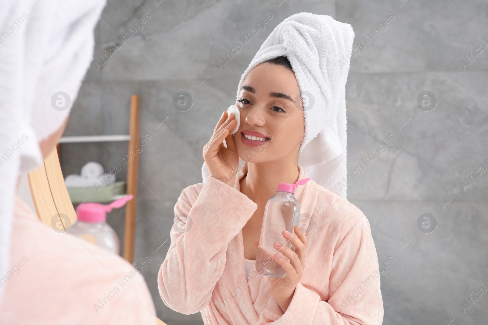 Photo of Beautiful woman in terry towel removing makeup with cotton pad near mirror indoors