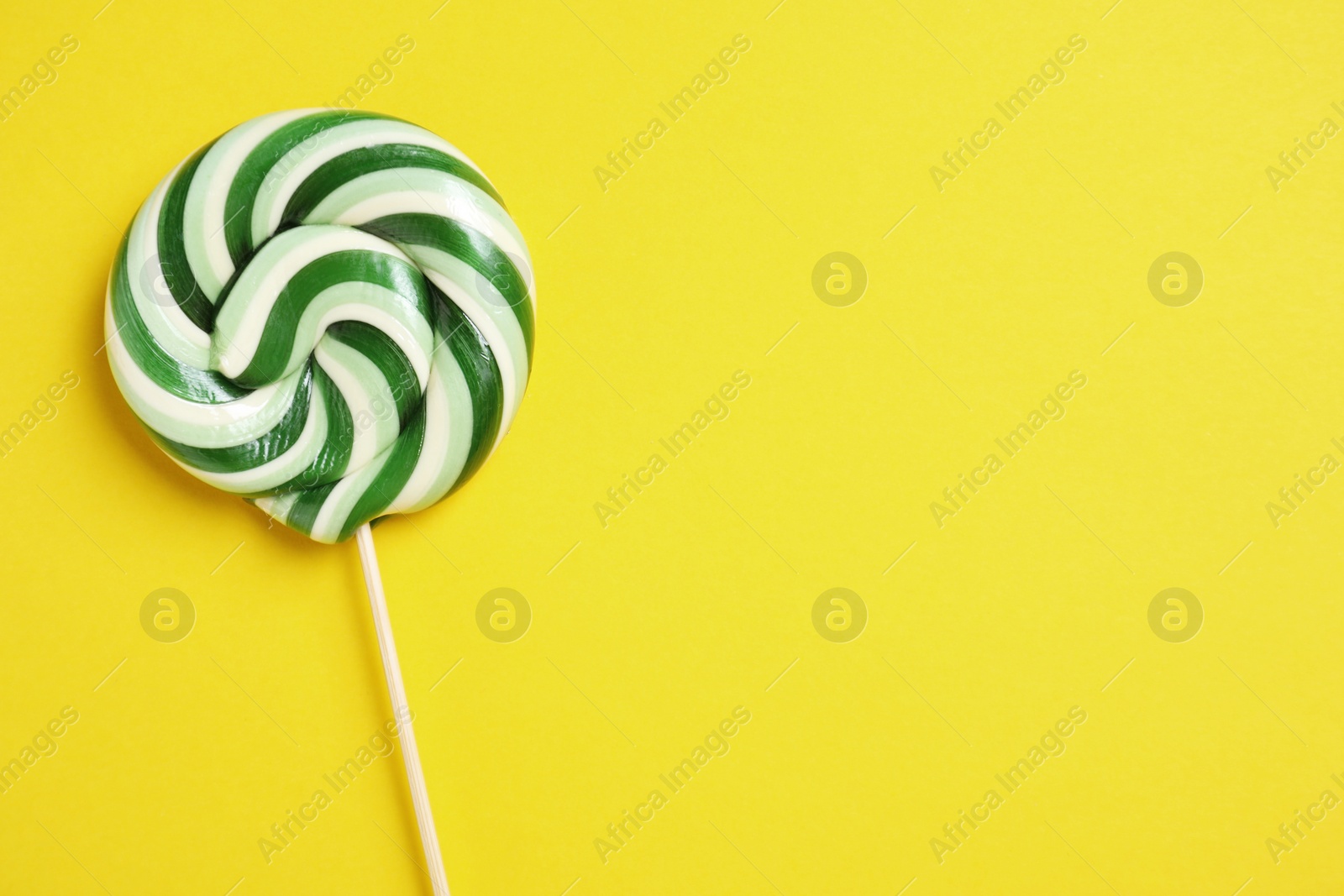 Photo of Stick with colorful lollipop swirl on yellow background, top view. Space for text