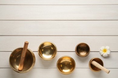 Golden singing bowls, mallets and flower on white wooden table, flat lay. Space for text