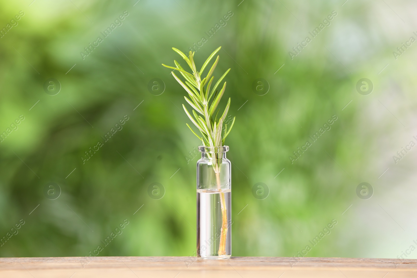 Photo of One bottle with essential oil and rosemary on wooden table against blurred green background