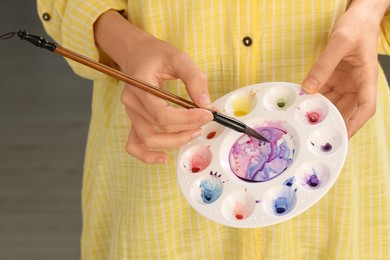 Photo of Woman mixing watercolor paints in art palette, closeup