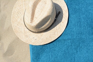 Photo of Soft blue beach towel with straw hat on sand, top view