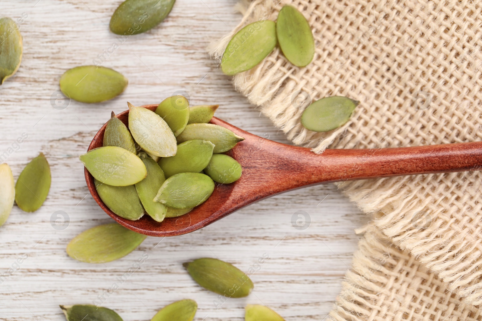 Photo of Spoon with peeled seeds on light wooden table, flat lay