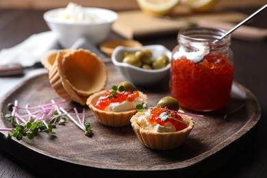 Photo of Delicious tartlets with red caviar and cream cheese served on wooden table, closeup