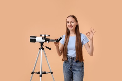 Photo of Happy astronomer with telescope showing OK gesture on beige background