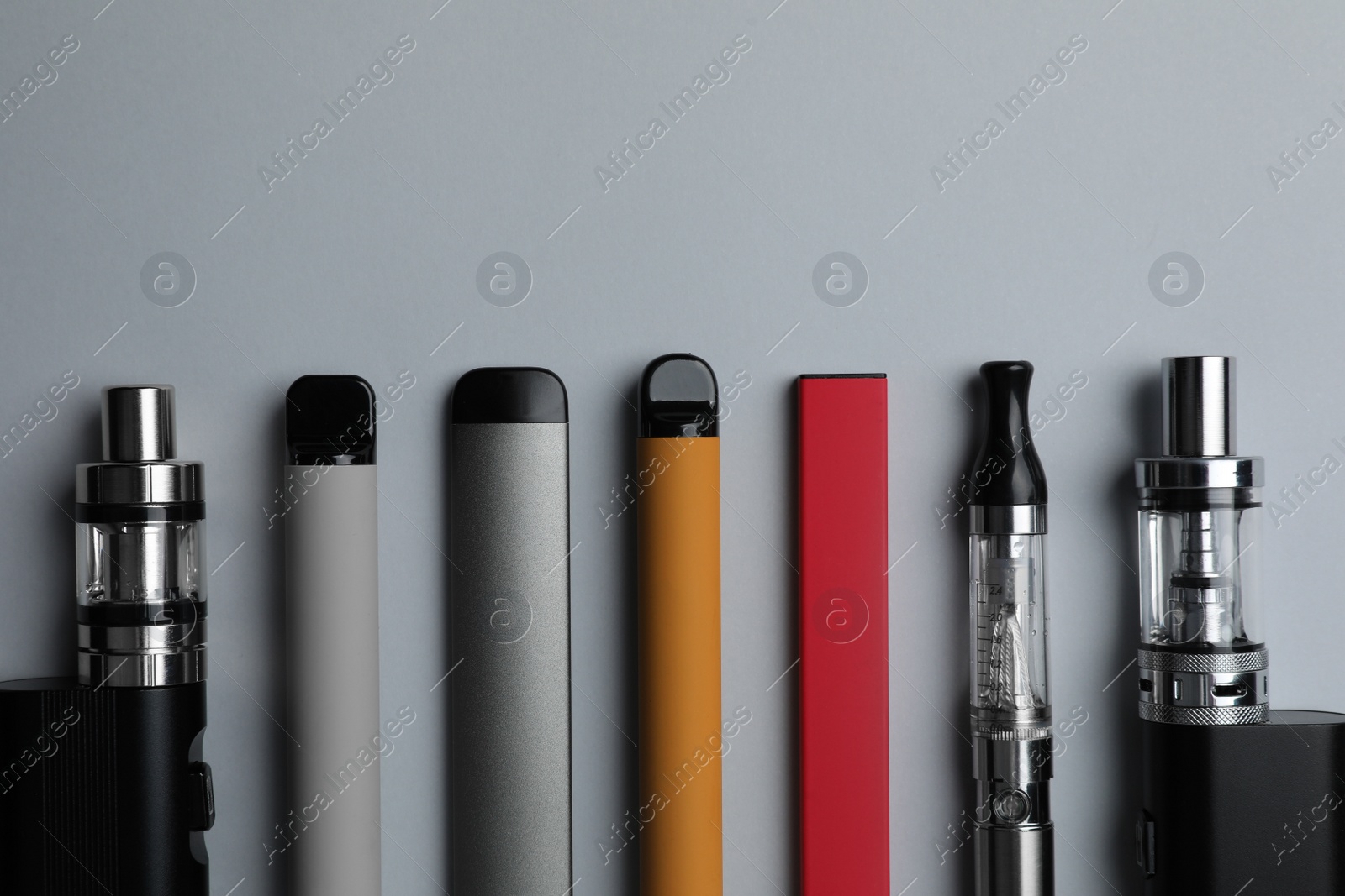 Photo of Many different electronic cigarettes on light background, flat lay