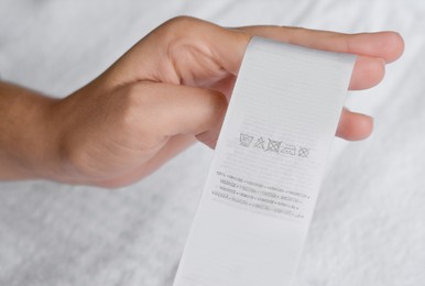 Photo of Woman holding clothing label on white garment, closeup