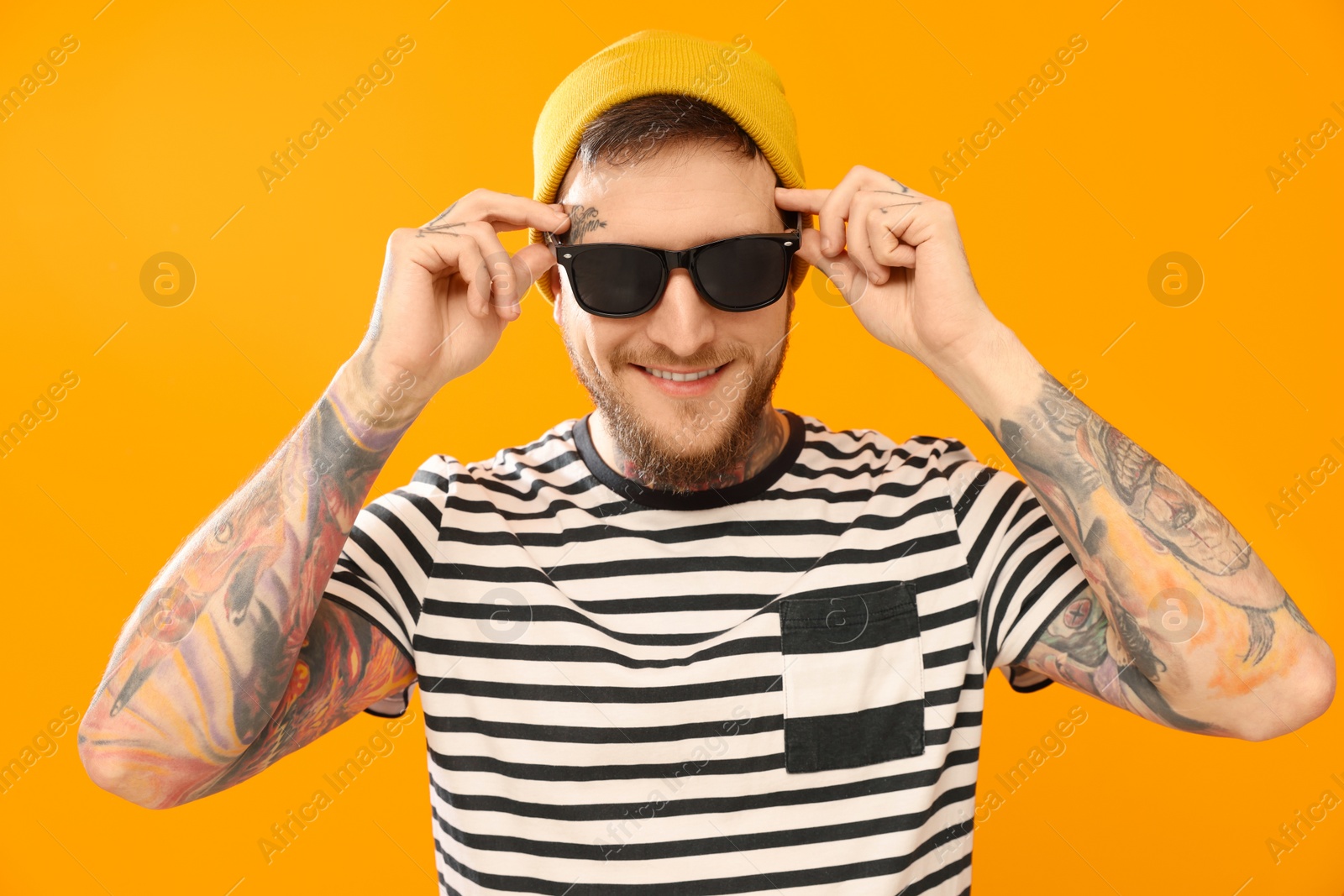 Photo of Handsome hipster man wearing stylish sunglasses on orange background