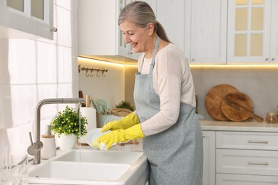 Happy housewife washing plate in kitchen sink