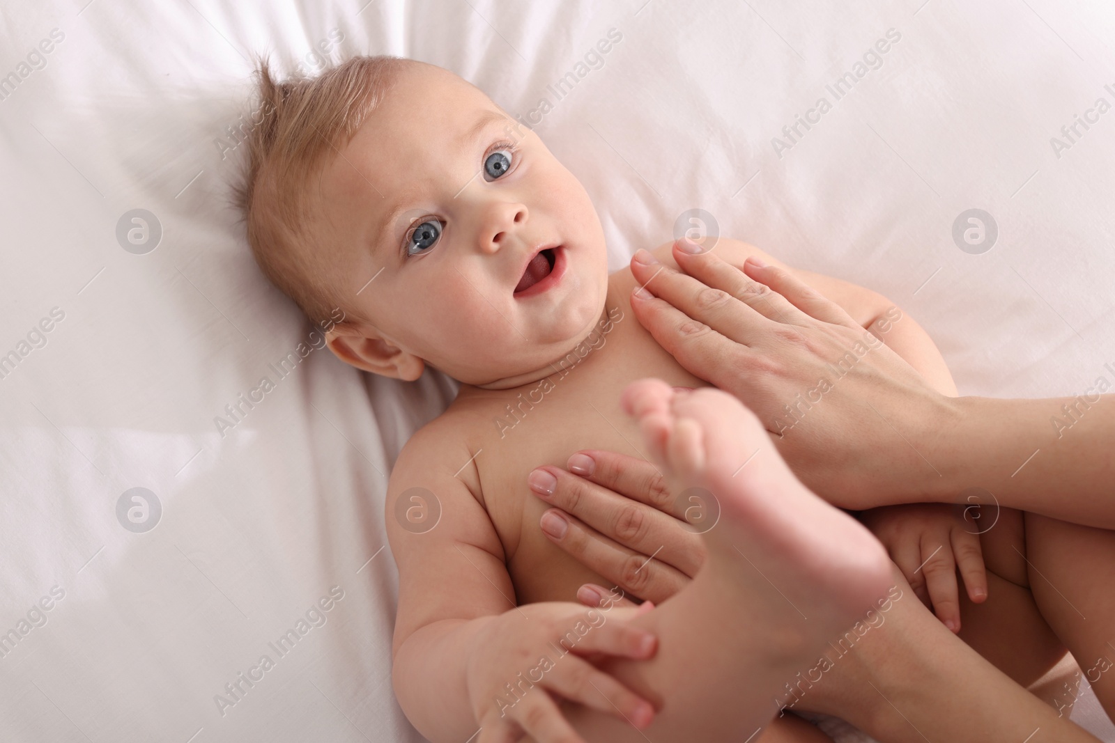 Photo of Mother massaging her cute baby with oil on bed, closeup