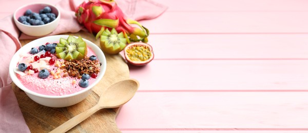 Image of Smoothie bowl with granola, kiwi and berries on pink wooden table. Banner design with space for text
