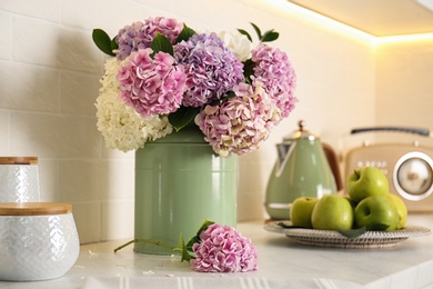 Photo of Beautiful hydrangea flowers in green can on light countertop, closeup