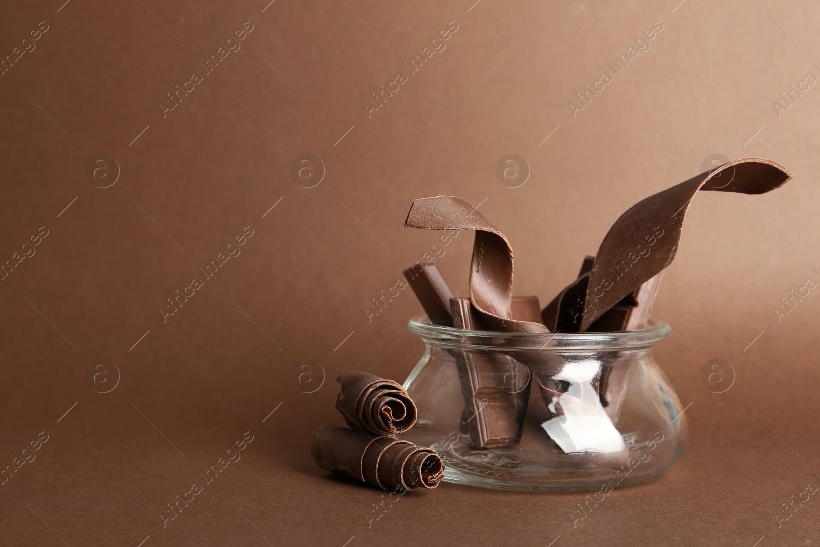 Photo of Glass jar with chocolate bars and curls on color background. Space for text