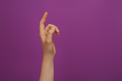 Woman showing index finger on purple background, closeup. Space for text
