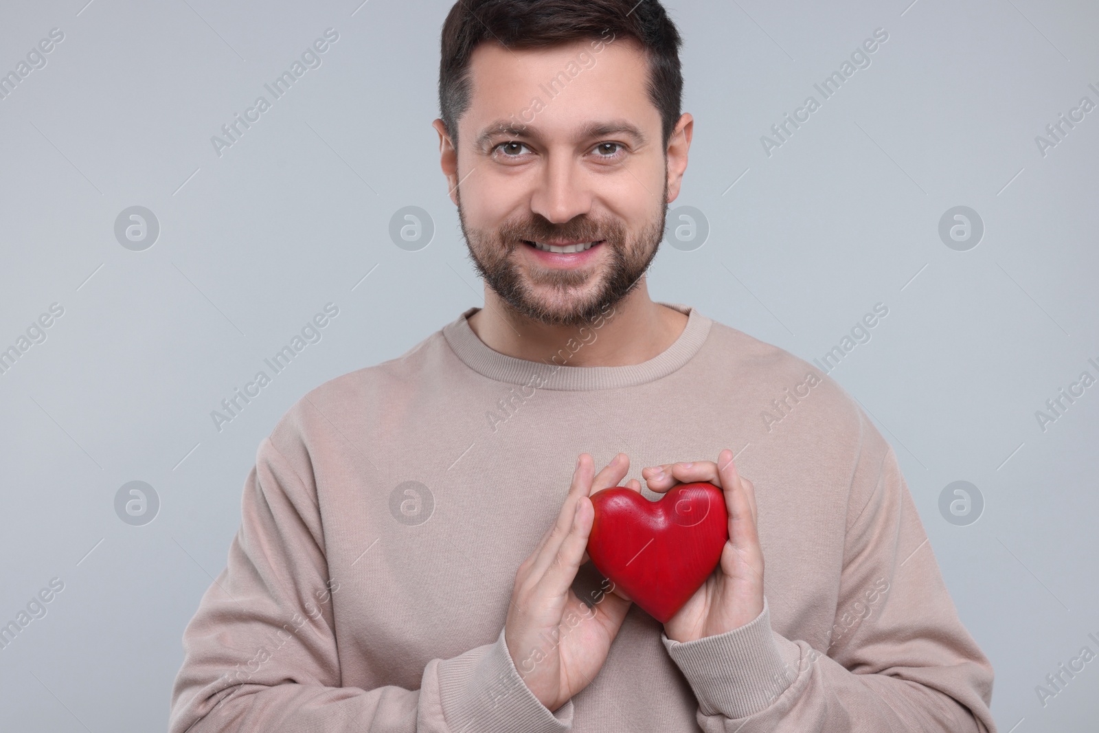 Photo of Happy man holding red heart on light grey background