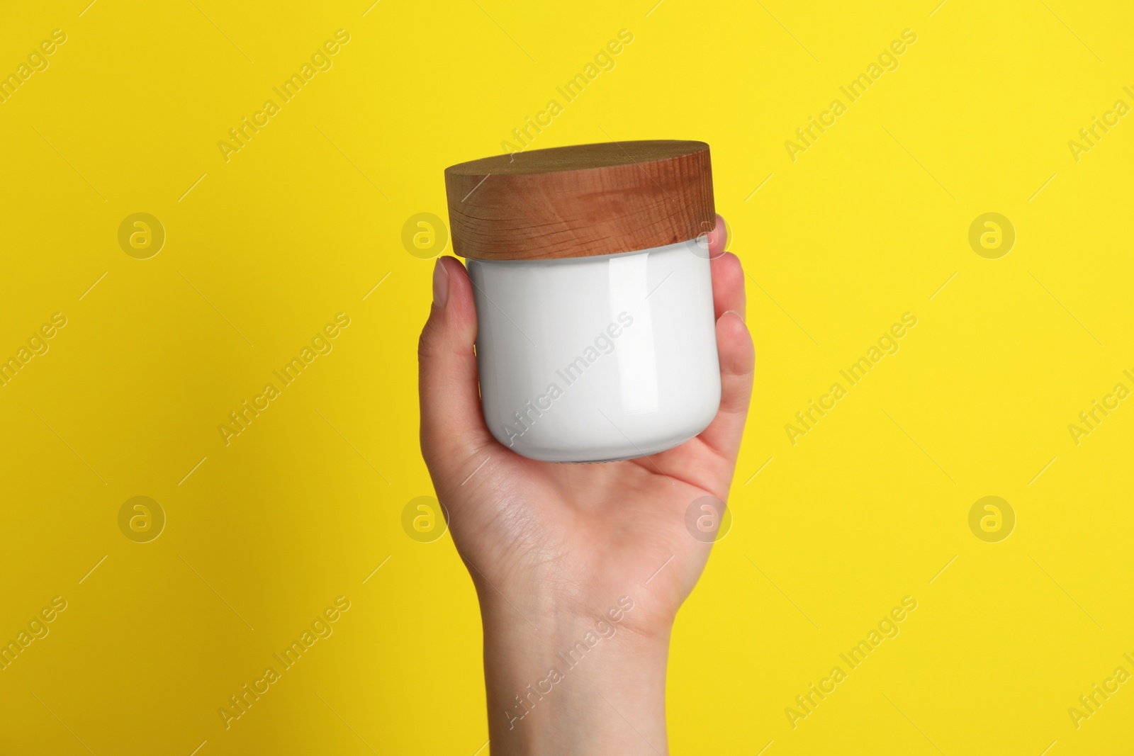 Photo of Woman holding jar of face cream on yellow background, closeup