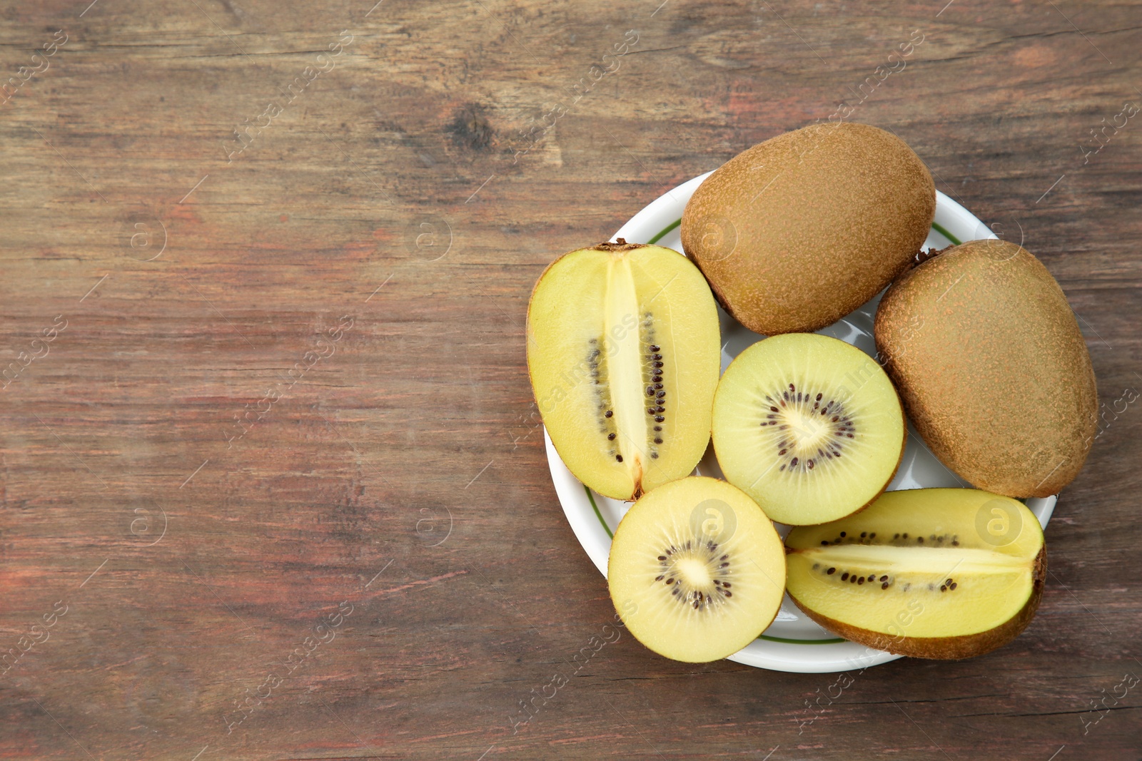 Photo of Plate with whole and cut fresh kiwis on wooden table, top view. Space for text