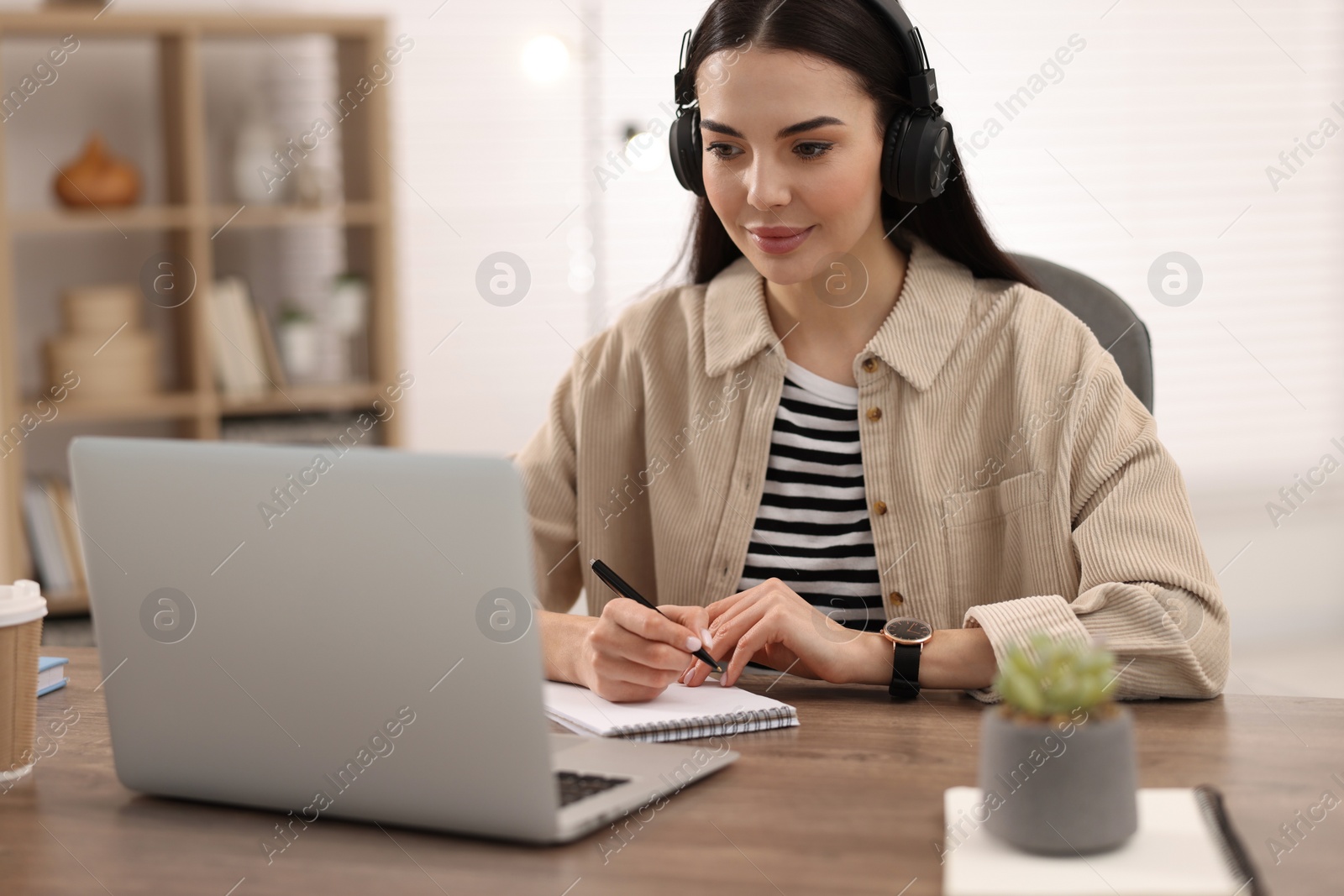 Photo of Young woman in headphones watching webinar at table in room