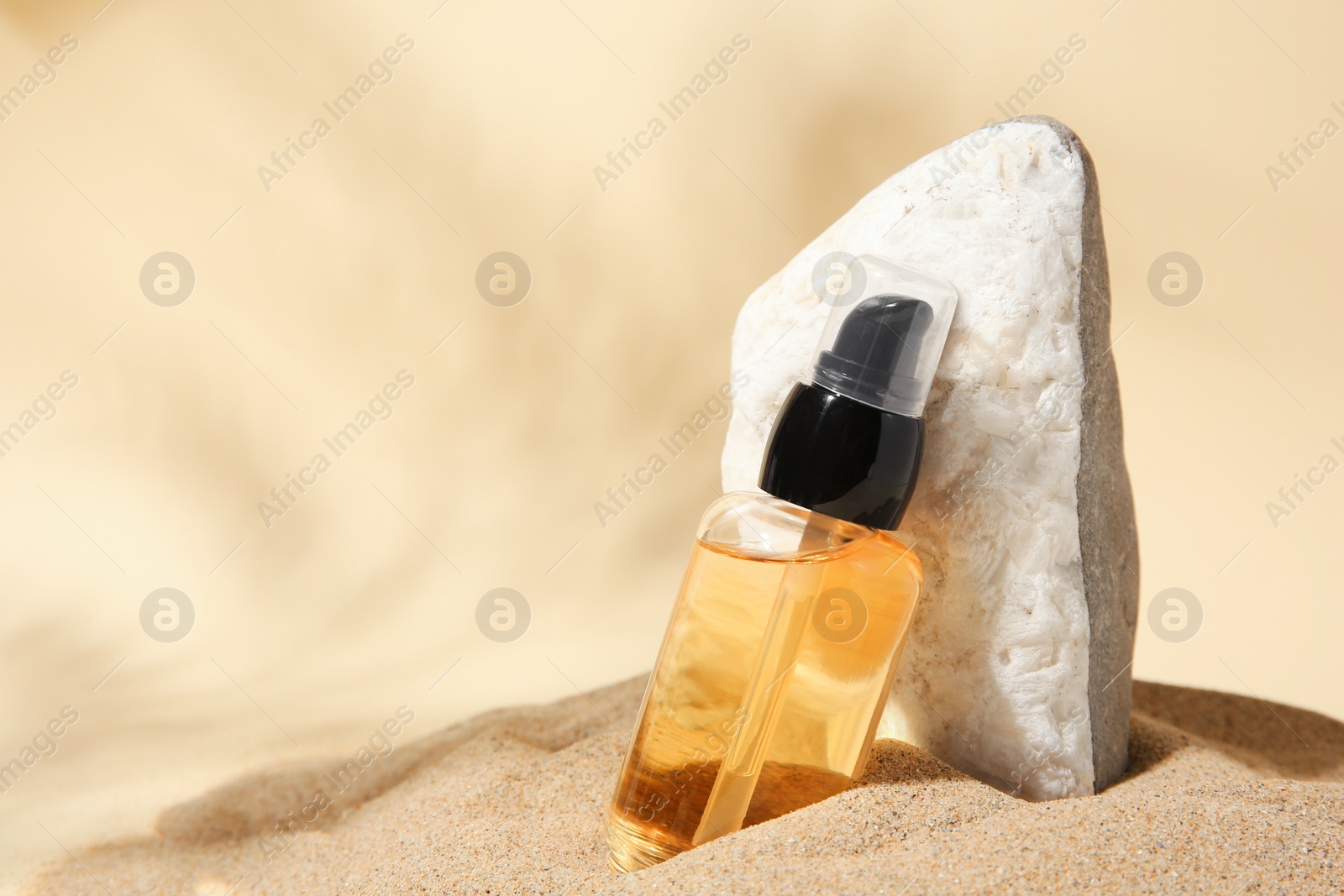 Photo of Bottle of serum and stone on sand against beige background. Space for text