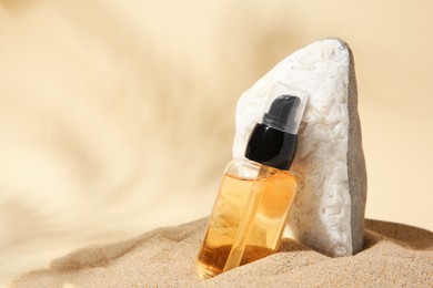 Bottle of serum and stone on sand against beige background. Space for text
