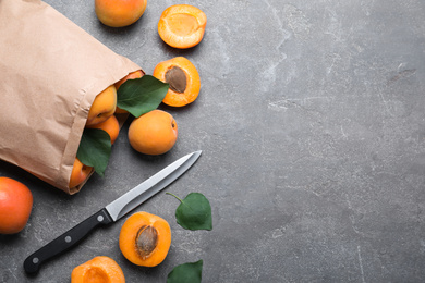 Many fresh ripe apricots and knife on grey table, flat lay. Space for text