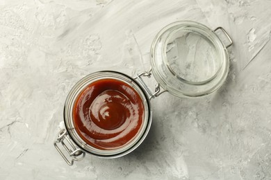 Photo of Tasty barbeque sauce in open jar on grey textured table, top view