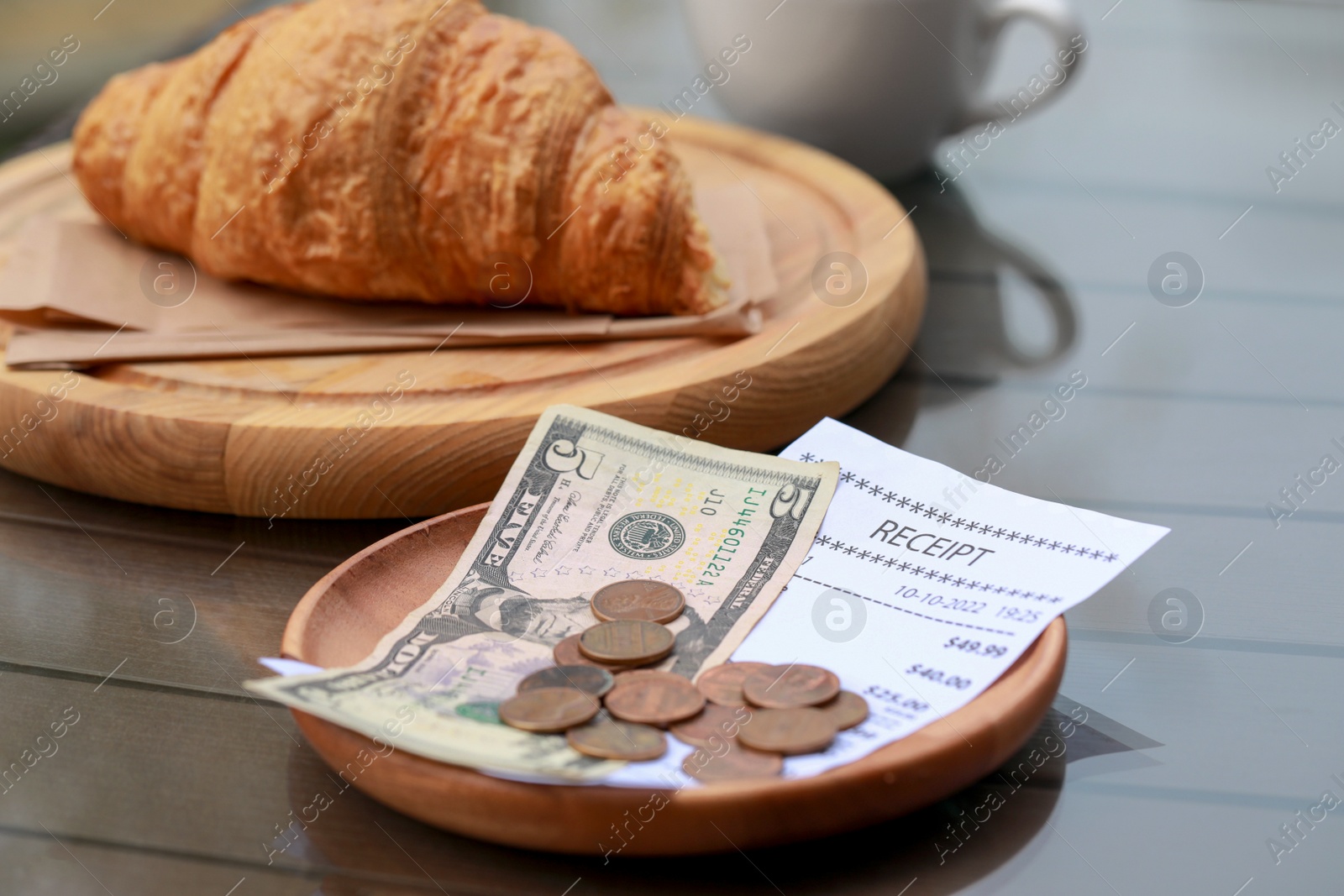 Photo of Tips, receipt and croissant on wooden table, closeup