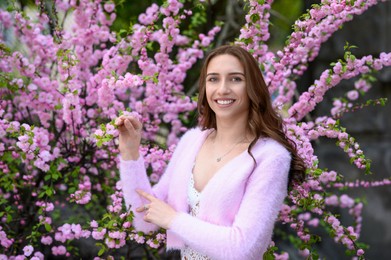 Beautiful young woman near blossoming sakura tree on spring day