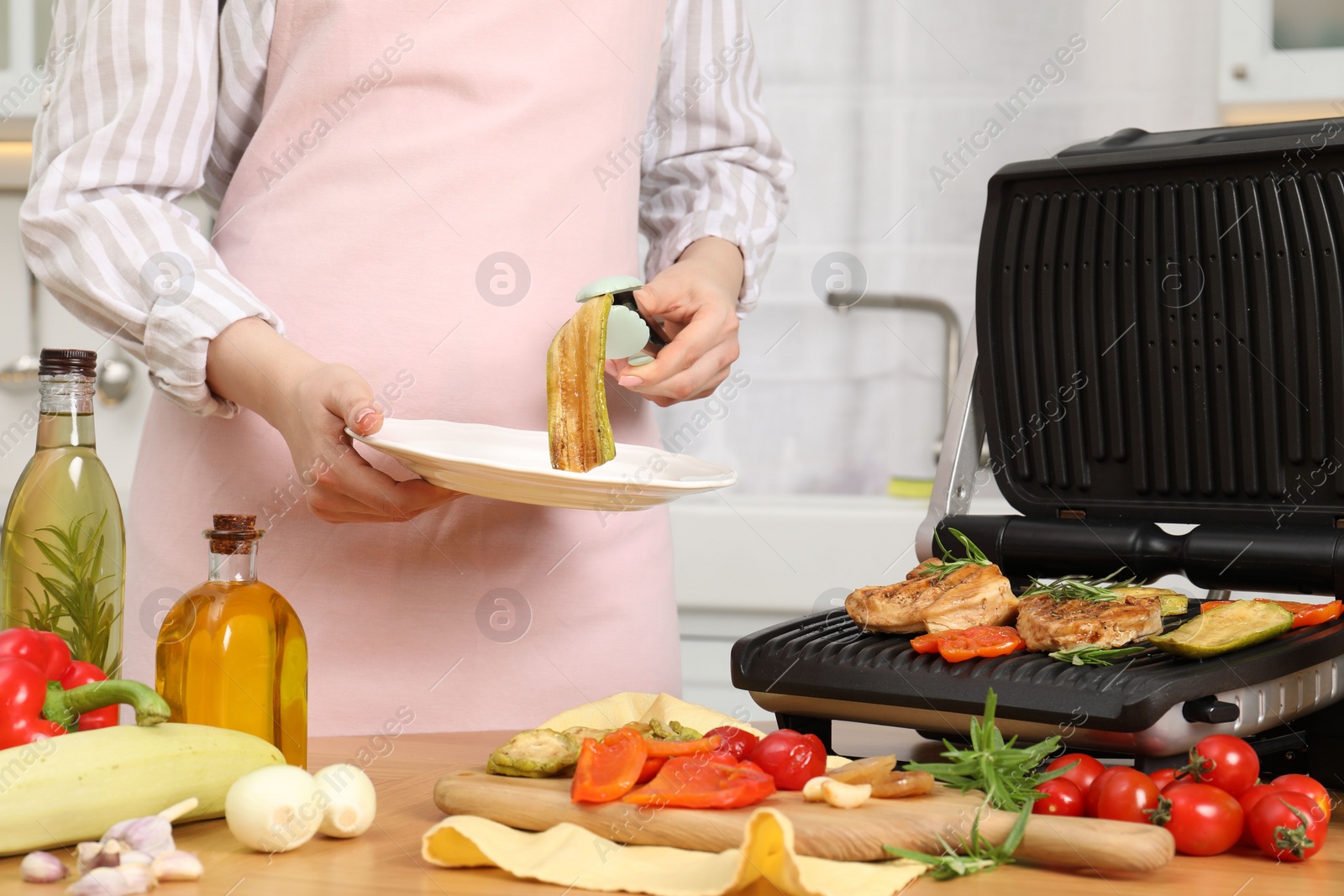 Photo of Woman cooking different products with electric grill at wooden table in kitchen, closeup