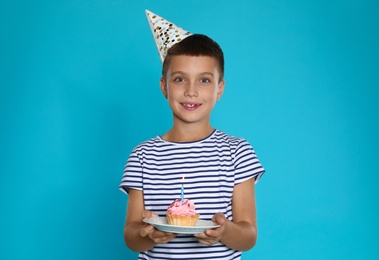 Happy boy holding birthday cupcake with candle on blue background