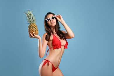 Beautiful woman in stylish bikini with pineapple on blue background. Space for text