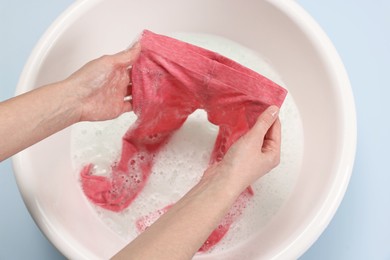 Photo of Woman washing baby clothes in basin on light blue background, above view