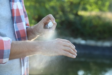 Photo of Man applying insect repellent onto hand outdoors, closeup