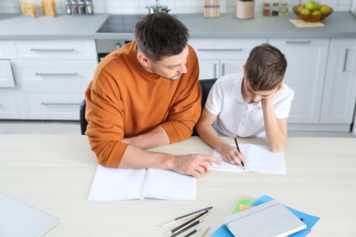 Photo of Dad helping his son with homework in kitchen, above view