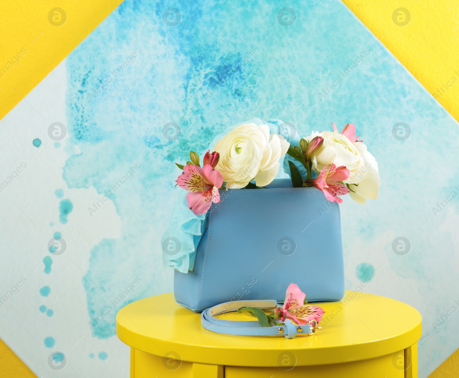 Photo of Elegant handbag with flowers and belt on table against color background