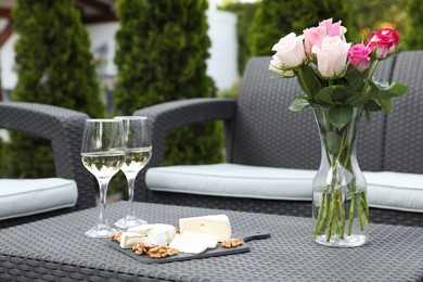 Photo of Vase with roses, glasses of wine and food on rattan table on outdoor terrace