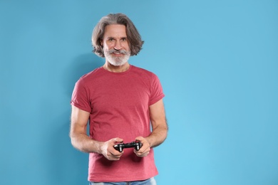 Photo of Emotional mature man playing video games with controller on color background. Space for text