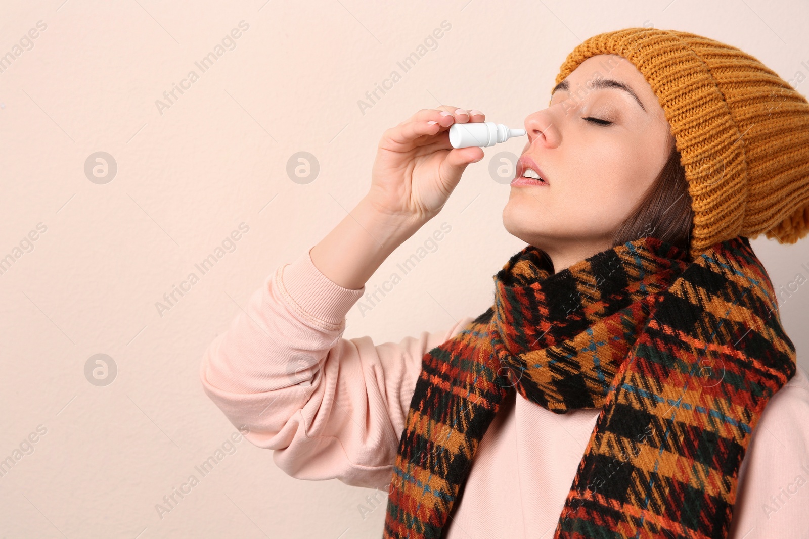 Photo of Woman using nasal spray on beige background, space for text