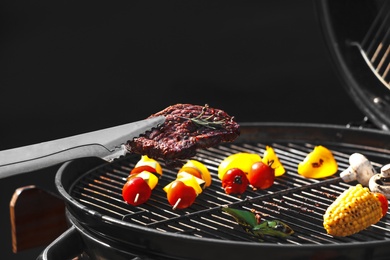 Photo of Tongs with tasty steak near modern barbecue grill