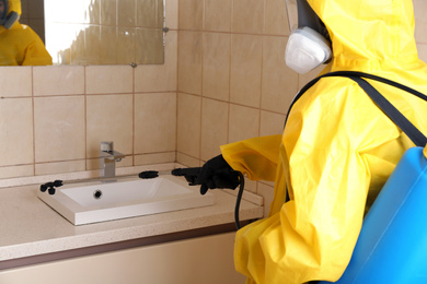 Photo of Pest control worker spraying pesticide near sink in restroom, closeup
