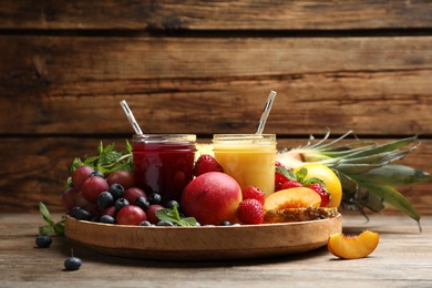 Photo of Delicious colorful juices in glasses and fresh ingredients on wooden table