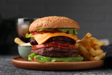 Photo of Tasty cheeseburger with patties, sauce and French fries on grey textured table, closeup