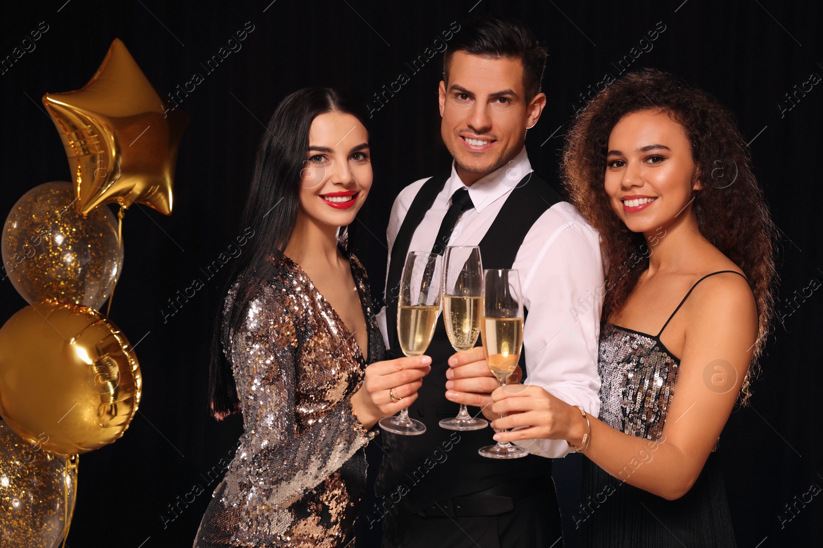 Photo of Happy friends with glasses of sparkling wine celebrating New Year on black background