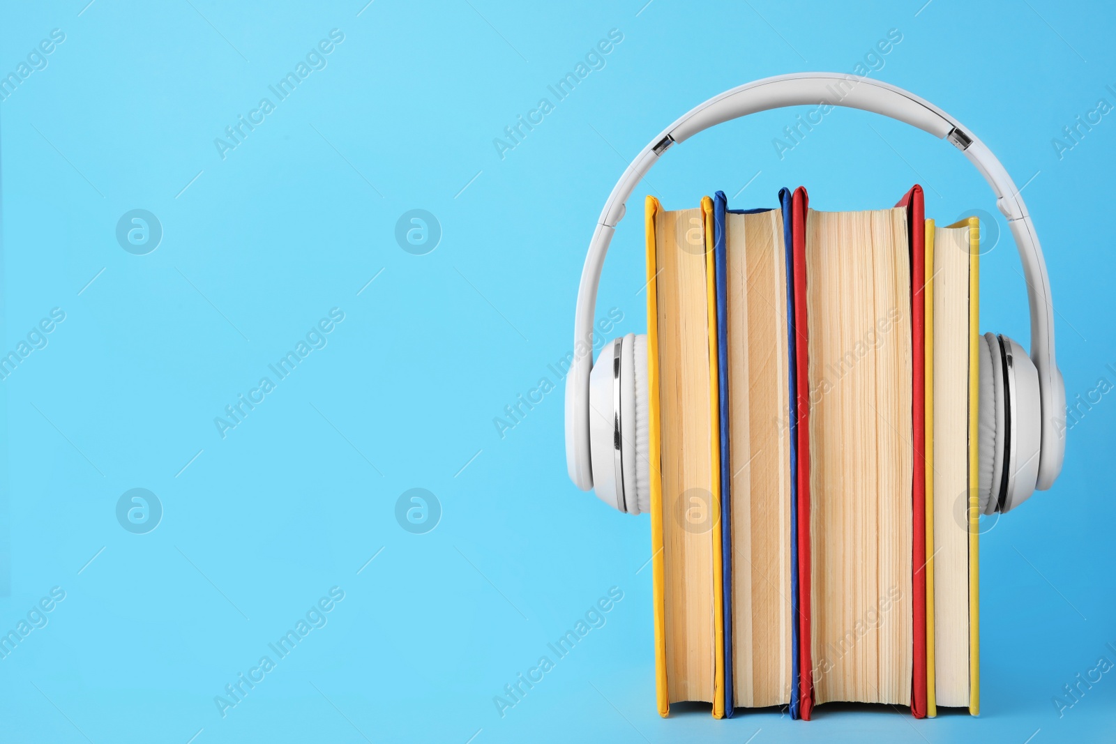 Photo of Books and modern headphones on light blue background. Space for text